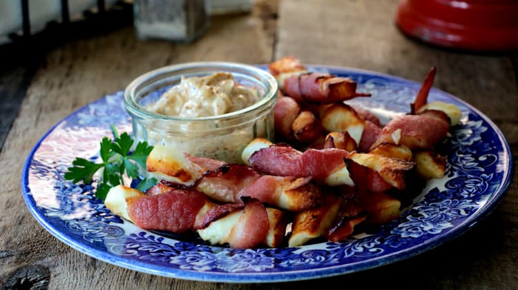 Assiette bleue sur planche de bois avec les collations de bacon et halloumi grillé