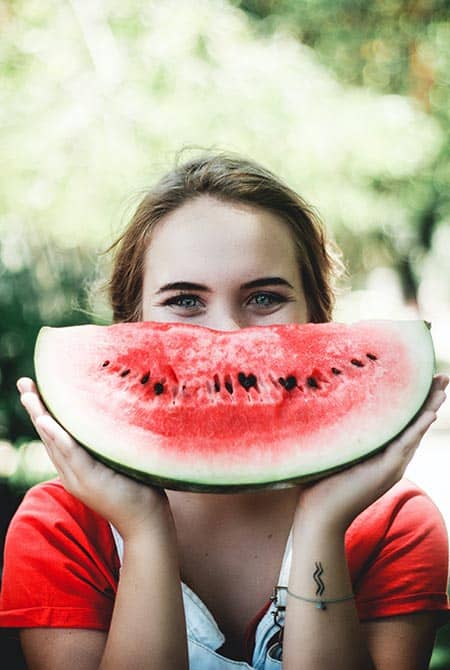 Jeune femme souriante avec un quartier de melon d'eau en guise de sourire